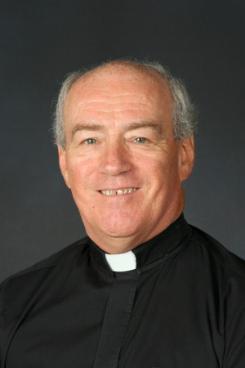 priest in black shirt in front of a gray backdrop